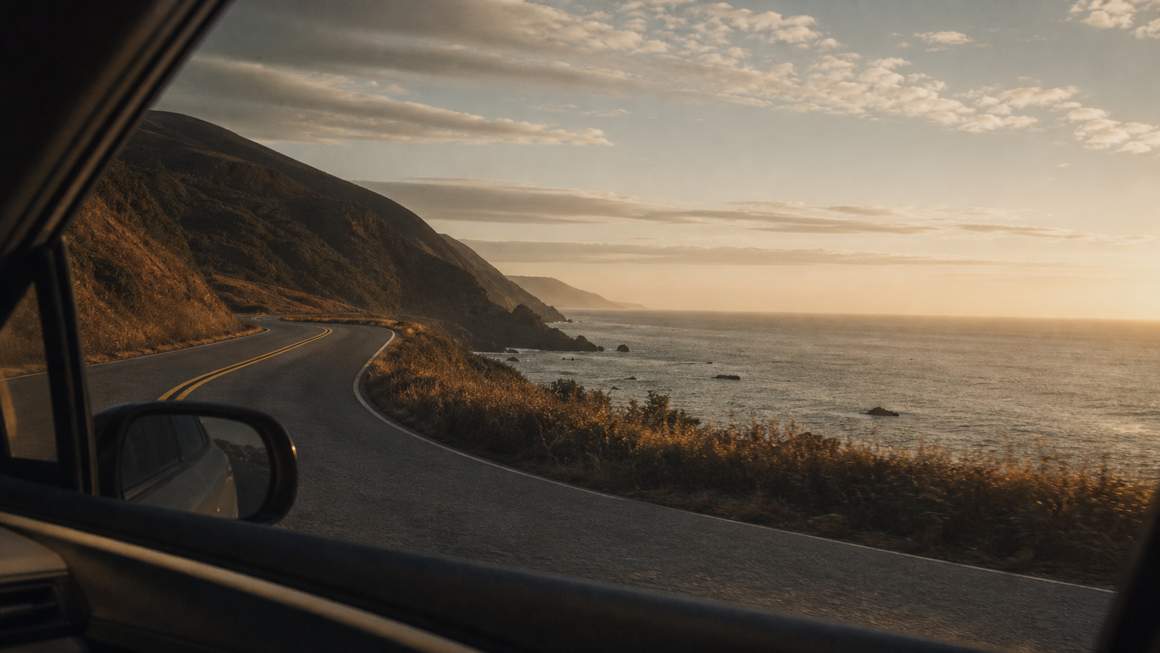 A coastal road at golden hour seen from a moving car window